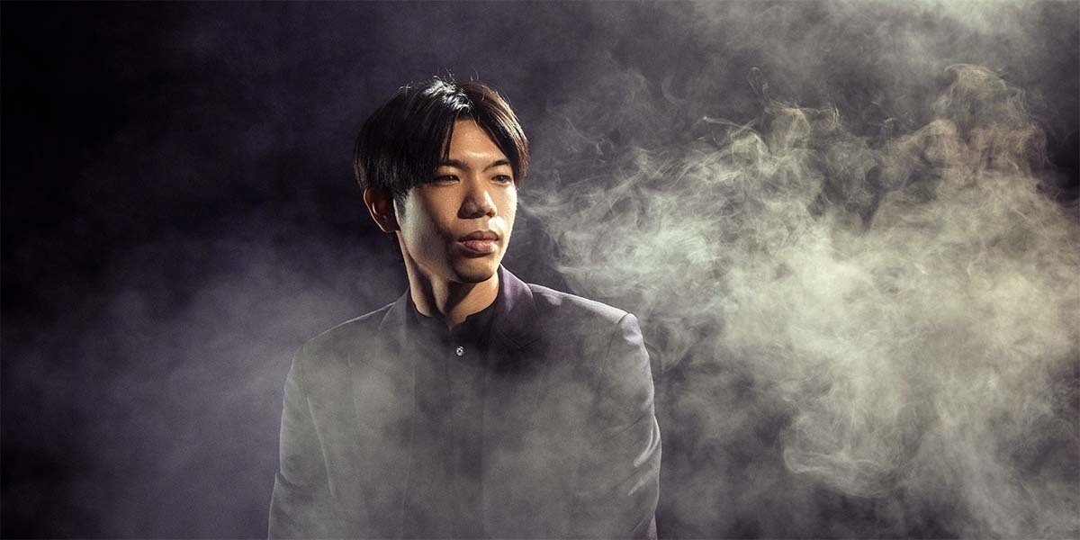 An Asian man looking sideways with wisps of smoke around him.