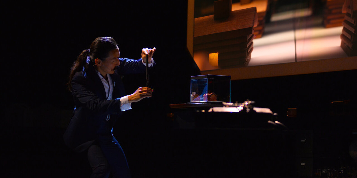 A man on a stage measures a miniature set on a table