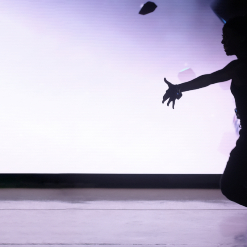 the shadow of a dancer in front of a screen showing her digital avatar