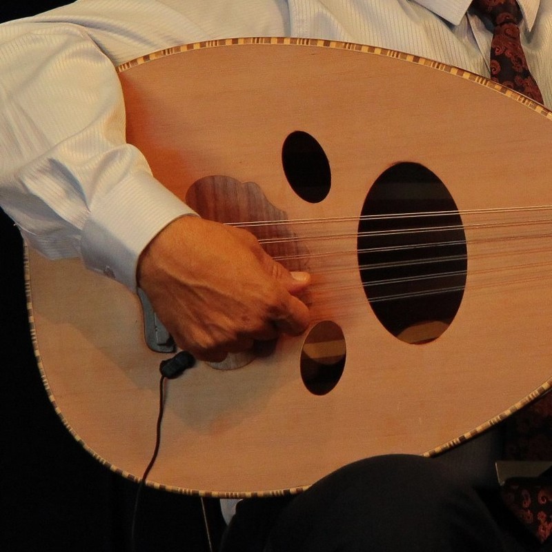 A close up photograph of a person playing a light brown guitar.