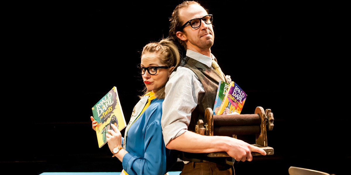 Two actors stand back to back with three Roald Dahl books in their hands