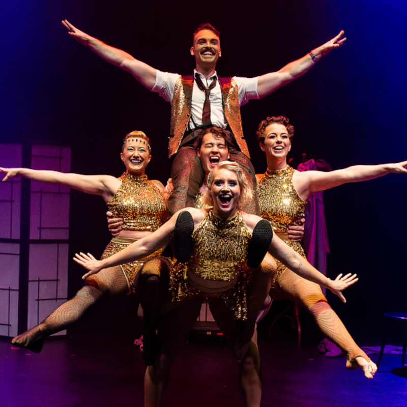 A group of acrobats in gold sparkly costumes build a human pyramid