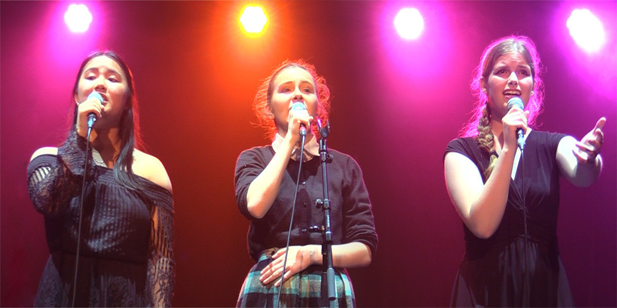 Image of 3 female singers holding microphones and singing