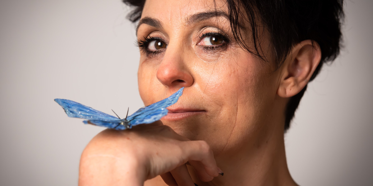 woman looking sad but hopeful, leaning on hand with a blue butterfly resting on it