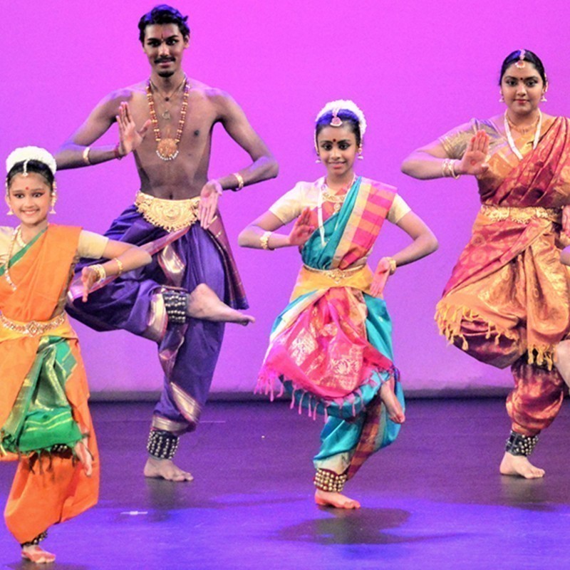 A photo of four Bharatanatyam dancers posing on stage in Indian cultural costumes.