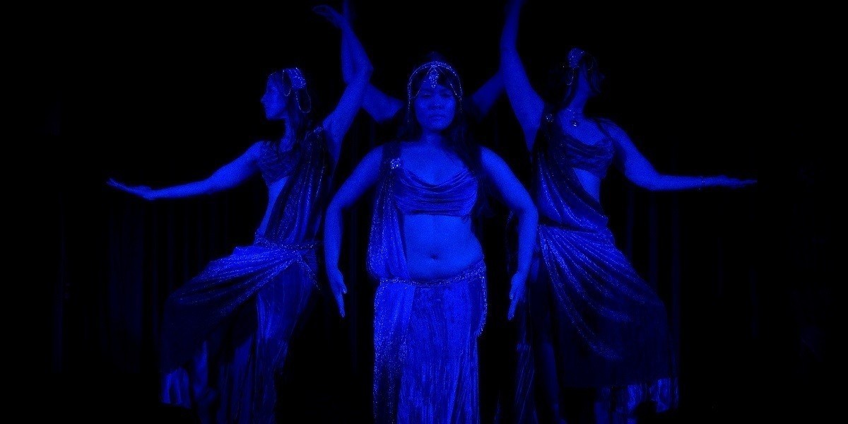 Four dancers in a symmetrical pose, wearing silver costumes in blue lighting, against a black backdrop. Representing the Moon card in a Tarot deck.
Central dancer with arms in downward curve, behind her dancer has arms raised, dancers on the sides have arms extended to the side in crescent shape, they represent the phases of the moon.