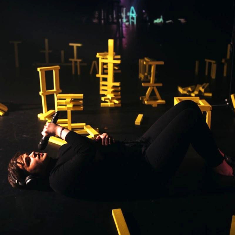 A person lying on a stage holding a microphone to their mouth surrounded by jenga blocks