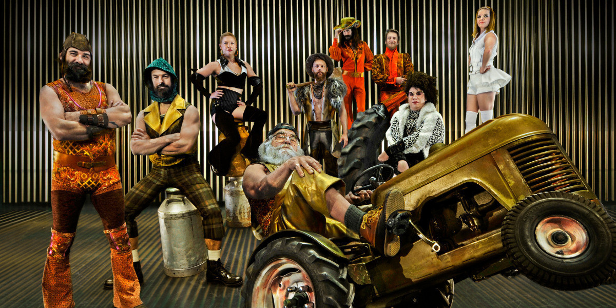 A group of circus performers in a barn posing around and on top of a tractor