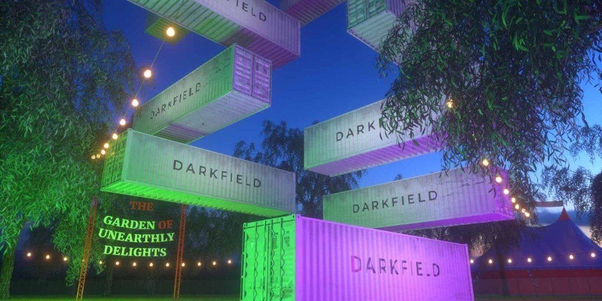 A festive fairy lit garden with shipping containers floating up in the air. It looks as if there was a stack of nine of them and they have begun floating upwards, leaving only one still on the ground. Each container has the word DARKFIELD written on it.