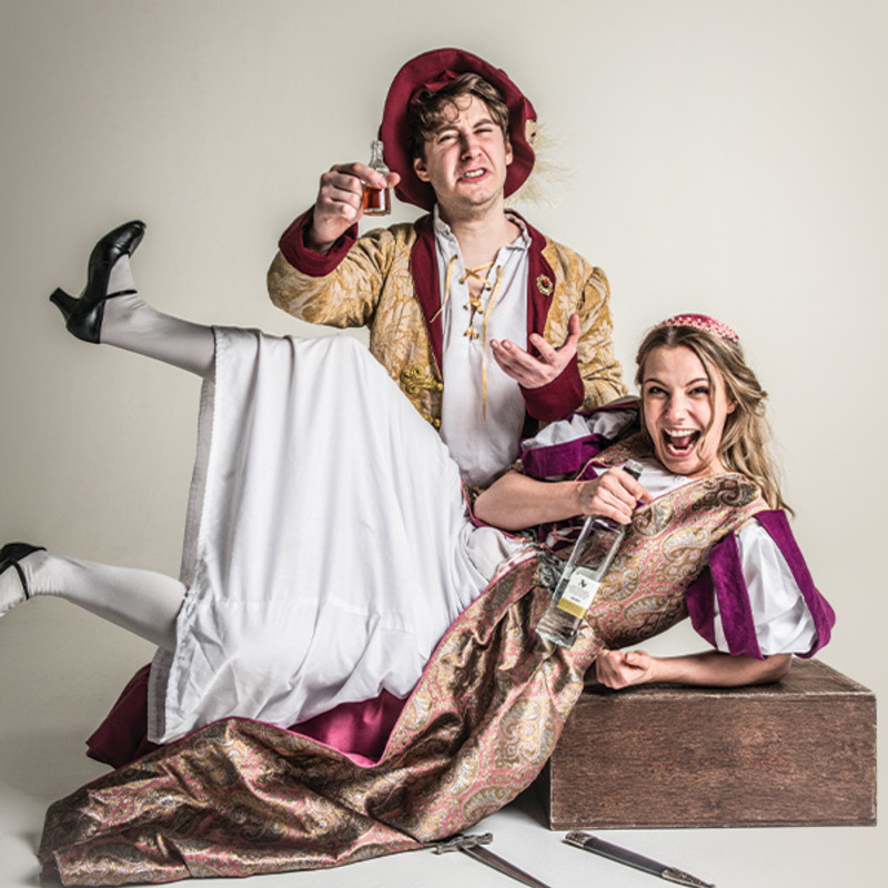A couple dressed as Romeo and Juliet on a white background, drinking wine