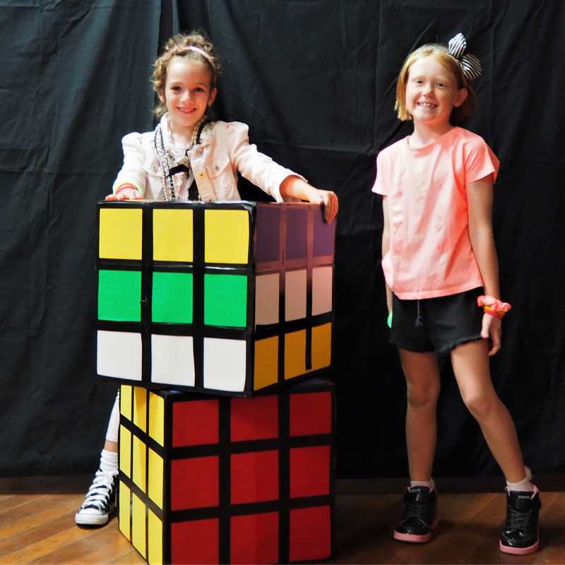 Retro Kids - Children in 80s themed costumes stand with giant Rubik's cubes.