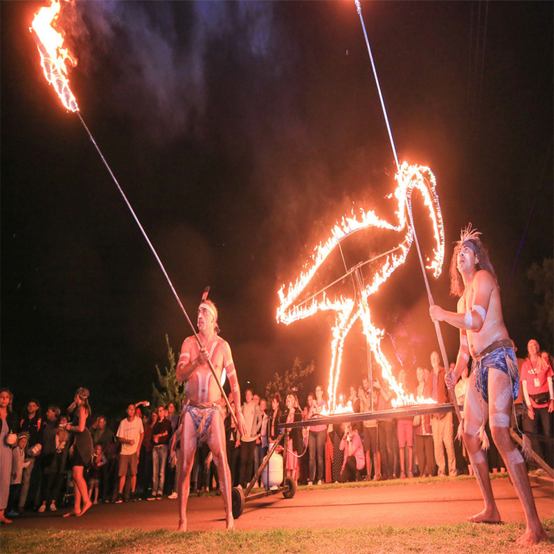 Yerta Palti Meyunna - Ceremony of People and Country - Two indigenous performers wearing traditional dress are holding large fire sticks and are standing next to  fire sculpture of an ibis. A large crown encircles the performers.