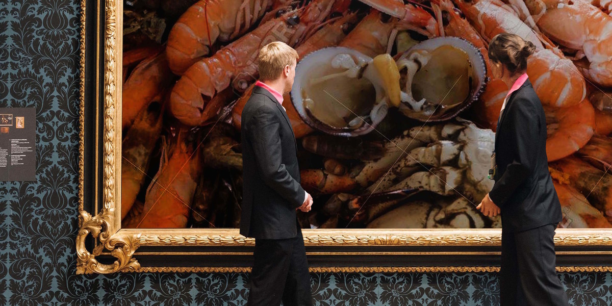 A man and woman dressed in suits look at a framed picture of seafood in an art gallery