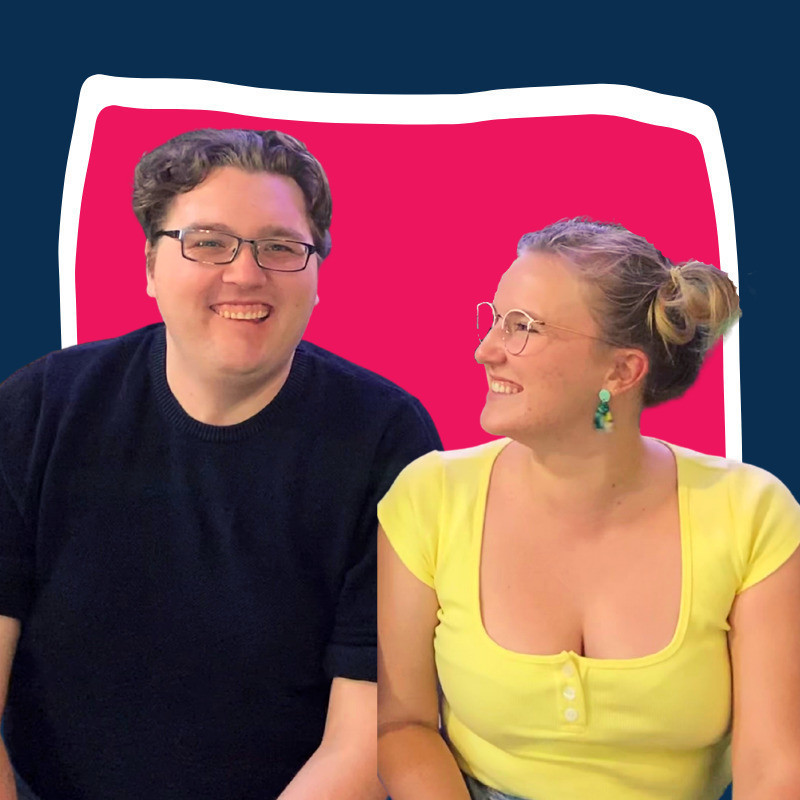 A photo of two people smiling. The person on the right is wearing a navy blue t-shirt and black framed glasses. The person on the right is wearing a yellow t-shirt, green earrings and clear framed glasses. The person on the right has their head turned to the person on the left.