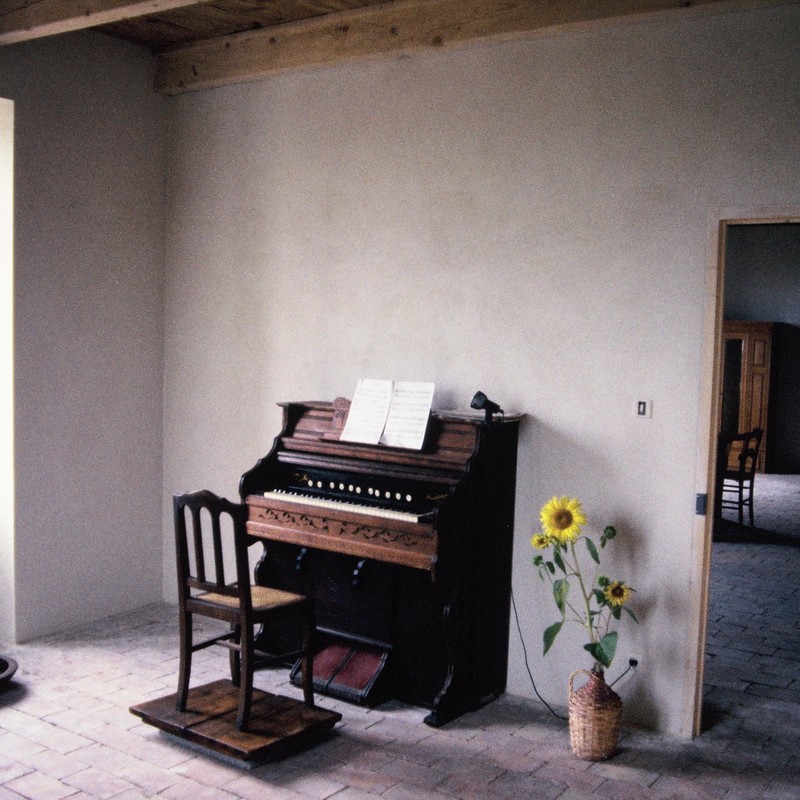 HEDDA, NORA, JULIE AND ME - A bare room. With an old upright piano. A sunflower in a vase. Floortiles and white walls.
