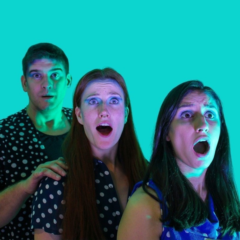 I'm A Raindrop, Get Me Outta Here! - Three people with surprised expressions stand diangonally in front of each other. They are all wearing matching dark blue tops with white polka dots. The teal background is a block colour, almost as if these people live in a two dimensional world.