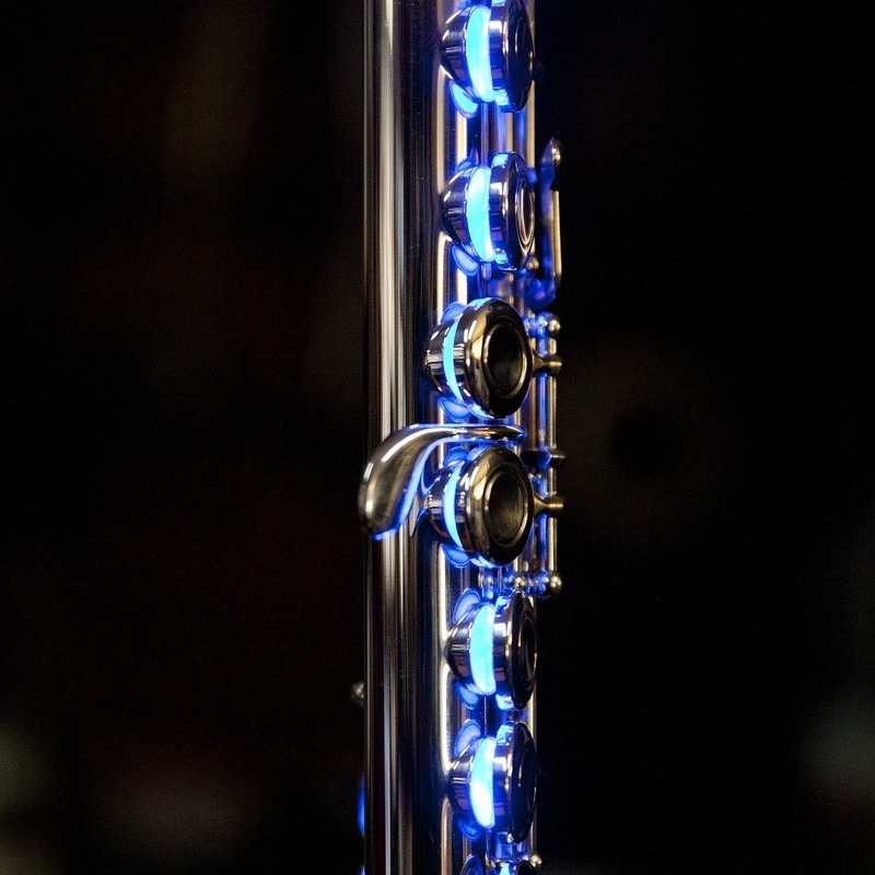 On Bright Air - The middle section of a flute with blue lighting coming through the keys on a black background