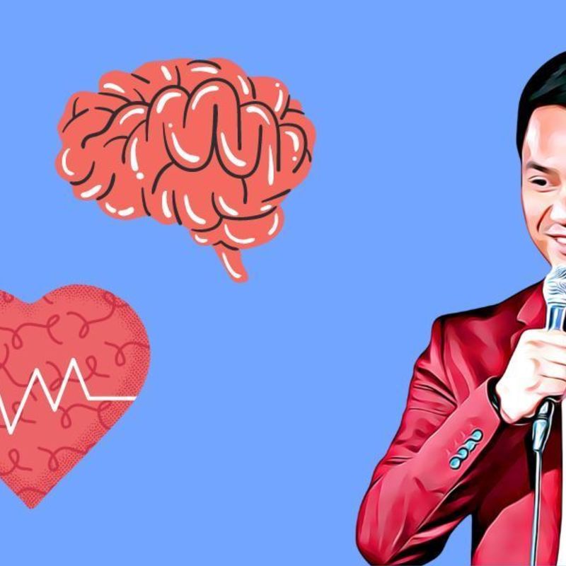 Doctor comedian Kim Le wearing a stethoscope and red suit jacket smiling whilst telling jokes into a microphone. Funny Medical related icons pill, brain and heart.