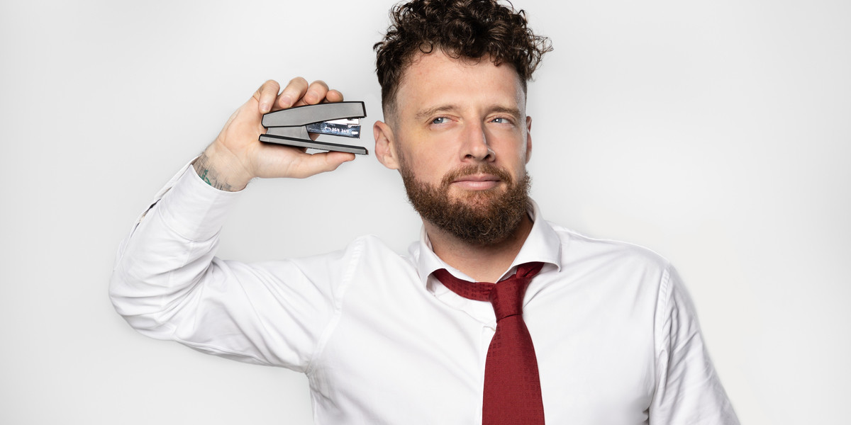 Comedian in red tie and white shirt holding stapler