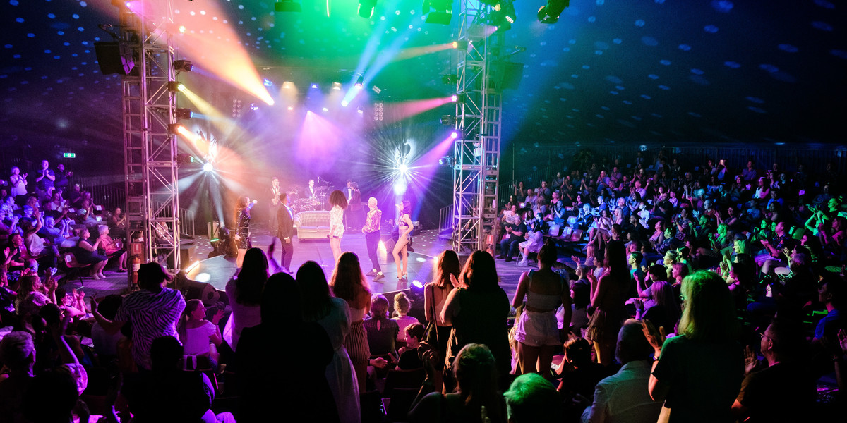 Disco Wonderland cast and band performing to a sold-out venue with audience members standing on their feet applauding.