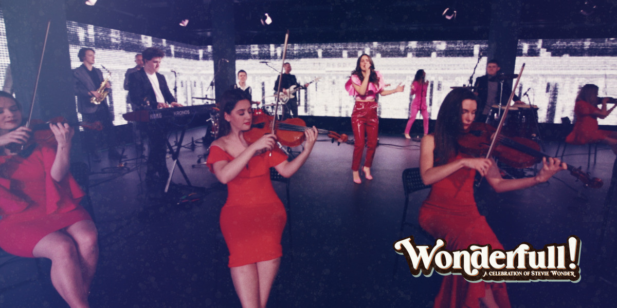 The Cast band in a group playing instruments on stage. All women are dressed in red and men dressed in black.