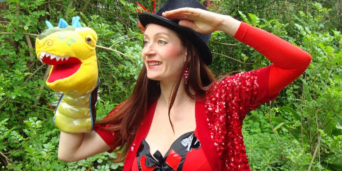 Jesstar is a lady wearing a top hat and a red jacket with a yellow dragon puppet on her hand.