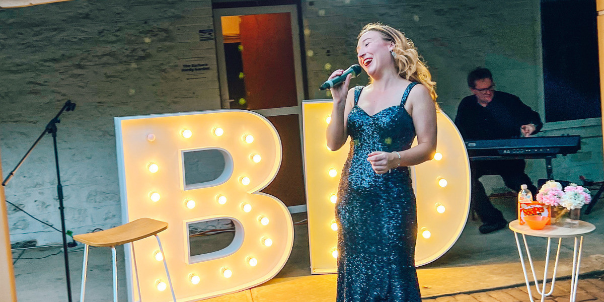 A performer sings into a microphone, in front of a light up letter B and D