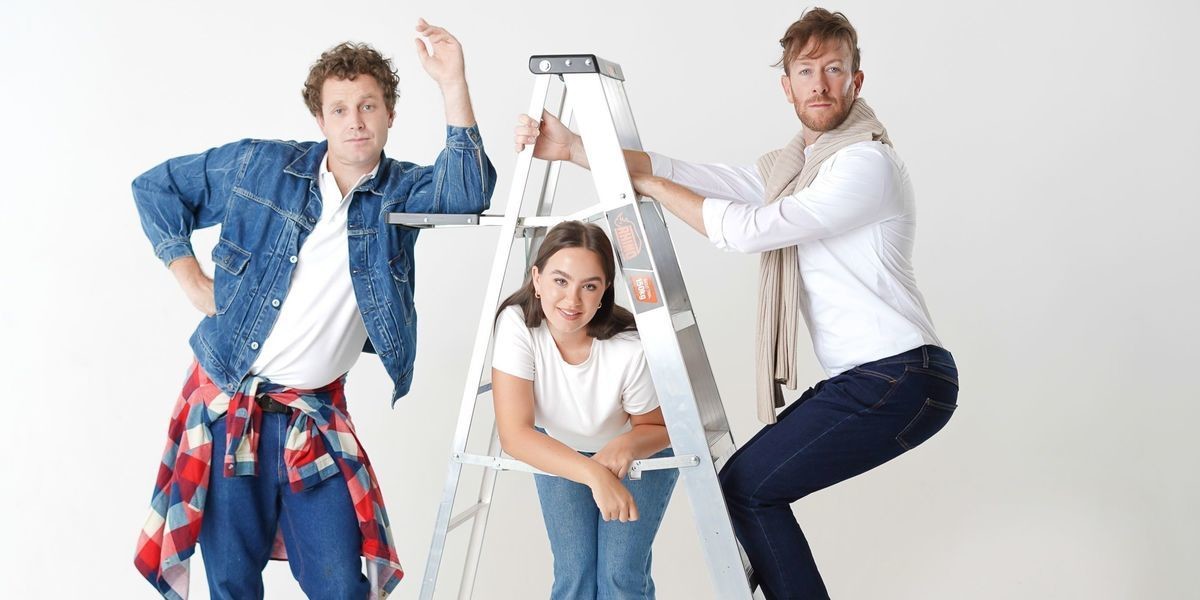 Two men leaning on a ladder & a woman underneath the ladder smiling at the camera.