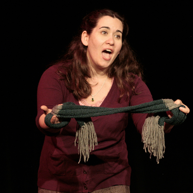 Brunette holding a green knitted scarf and singing.