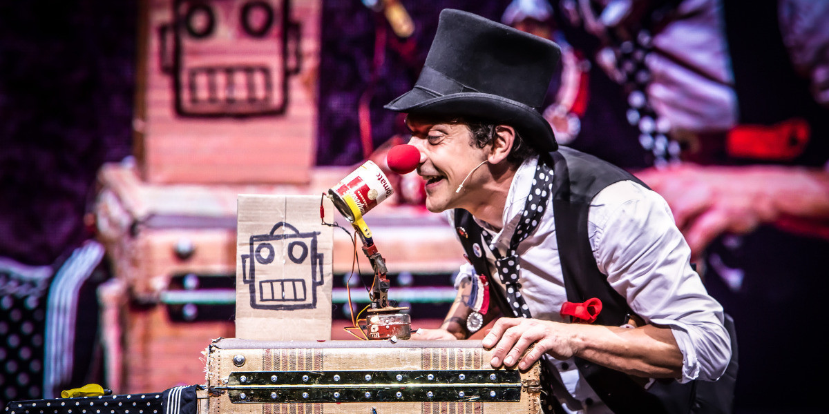 Mario the Maker Magician onstage with robot and magic props from the show wearing a clown red nose
