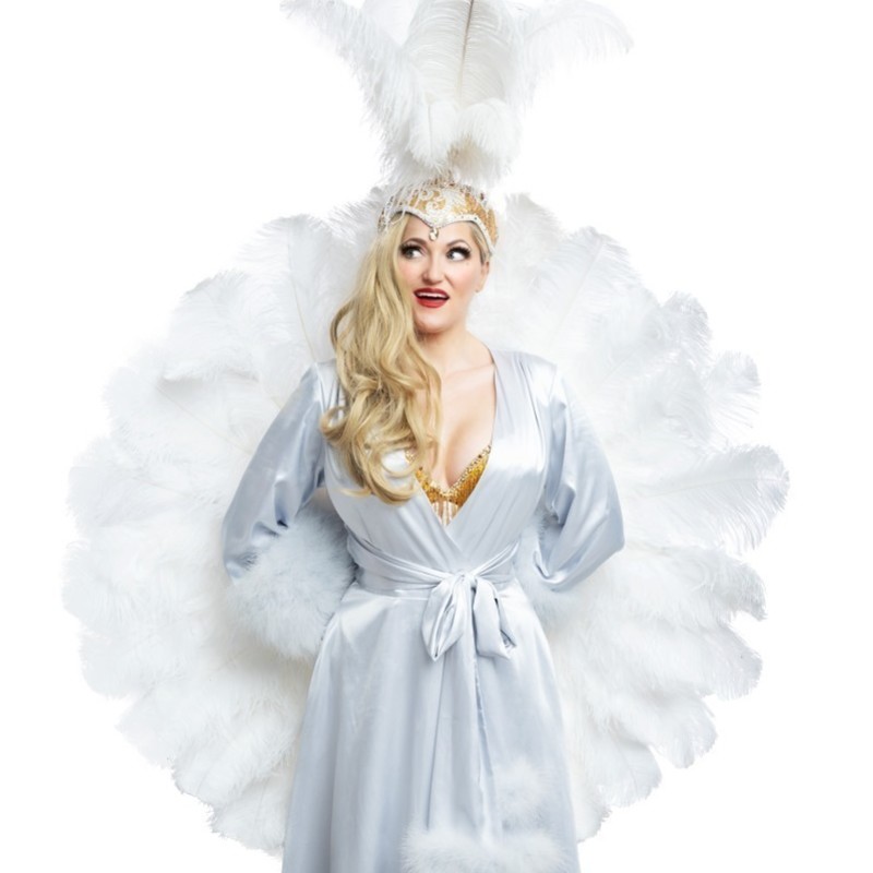Diva Student Showcase - Blonde burlesque performer in white feathered headdress and silver gown holding a pair of white feather fans and looking to the left with a smile.