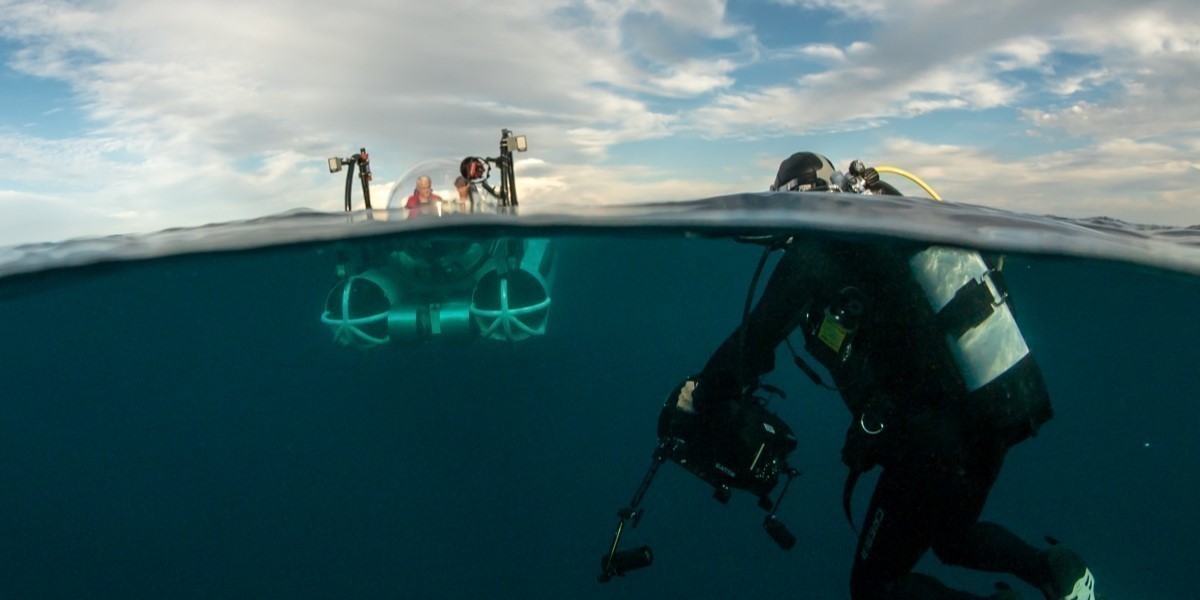 Camera crew on the surface of the ocean and a camera man in diving gear underneath the surface.
