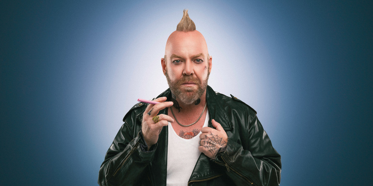Pete stands in front of a blue and white backdrop, staring intensely into the camera. He is dressed as a biker-punk, with a leather jacket and mohawk
