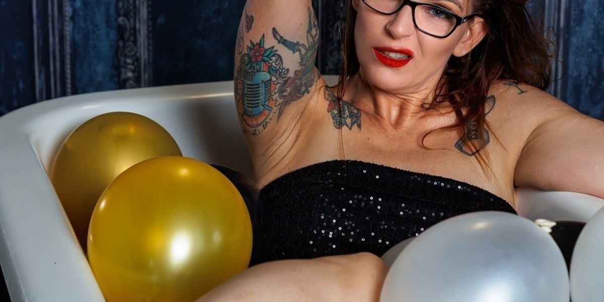 Vivienne Starr, sitting in a bathtub filled with balloons, with a sexy snarling face & messy hair