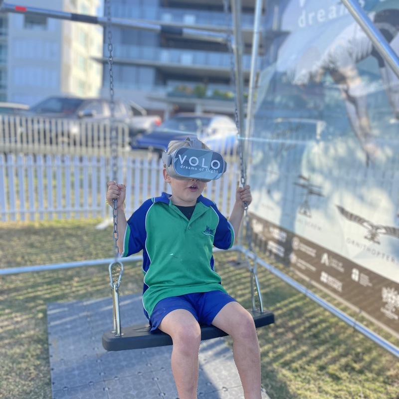 Young child swinging on a swing and wearing VR headset.