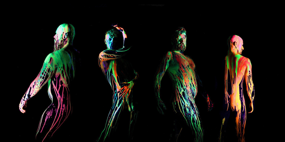 Moist - four male bodies, are silhouetted on a black background, each body is covered in neon bright paint dripping down their skins. they are standing various poses, highlighting their different body shapes and proportions.