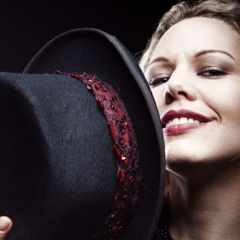Malin Nilsson smiling whilst holding a top hat mysteriously