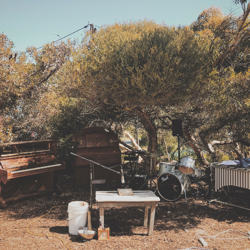 Emerging Composers Forum Concert - Musical instruments, including a piano, harmonium, drum kit, vibraphone, and amplified percussion, set up outside under the canopy of the Aldinga scrub.
