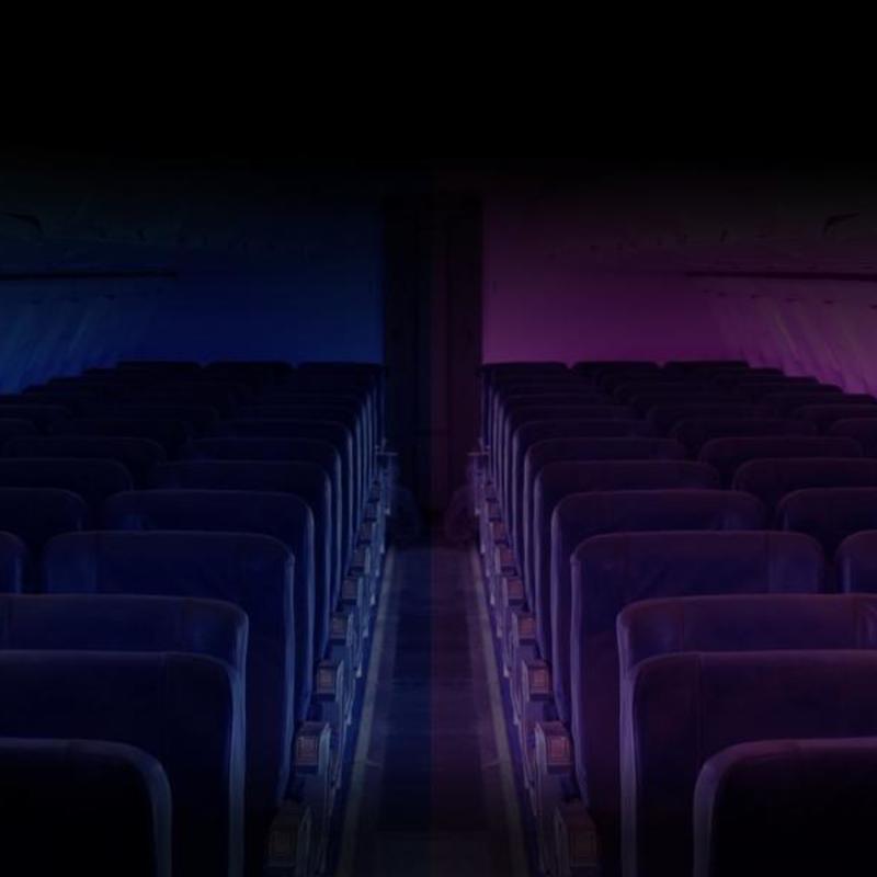 A landscape shot of a plane interior. The left side of the plane is a dark blue colour and the right half of the plane is a pinky purple colour.