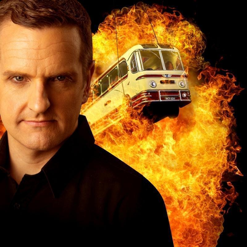 A serious brown-haired man stares at the viewer. Behind him is an explosion, out of which emerges a toy bus, held up with strings.