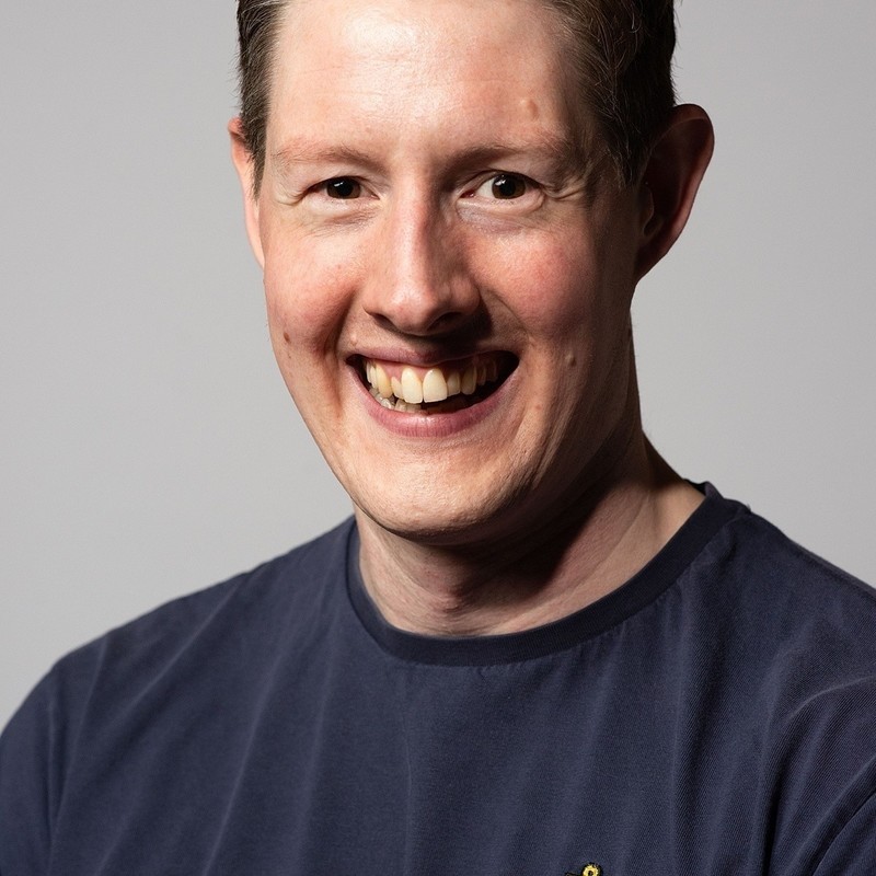 A photo of a person smiling. They are wearing a grey t-shirt.