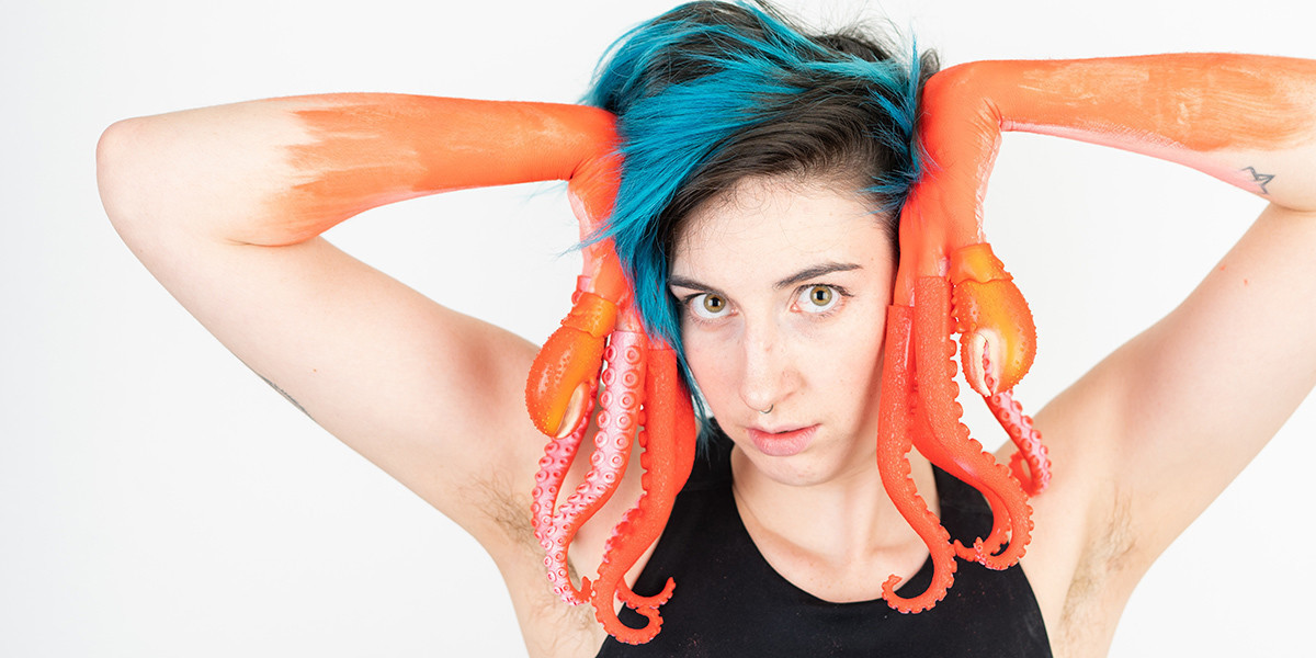 A person with blue pixie-cut hair has pink-orange tentacles instead of hands. They pose framing their face with the tentacles, vogue-style, a serious model expression. White background.