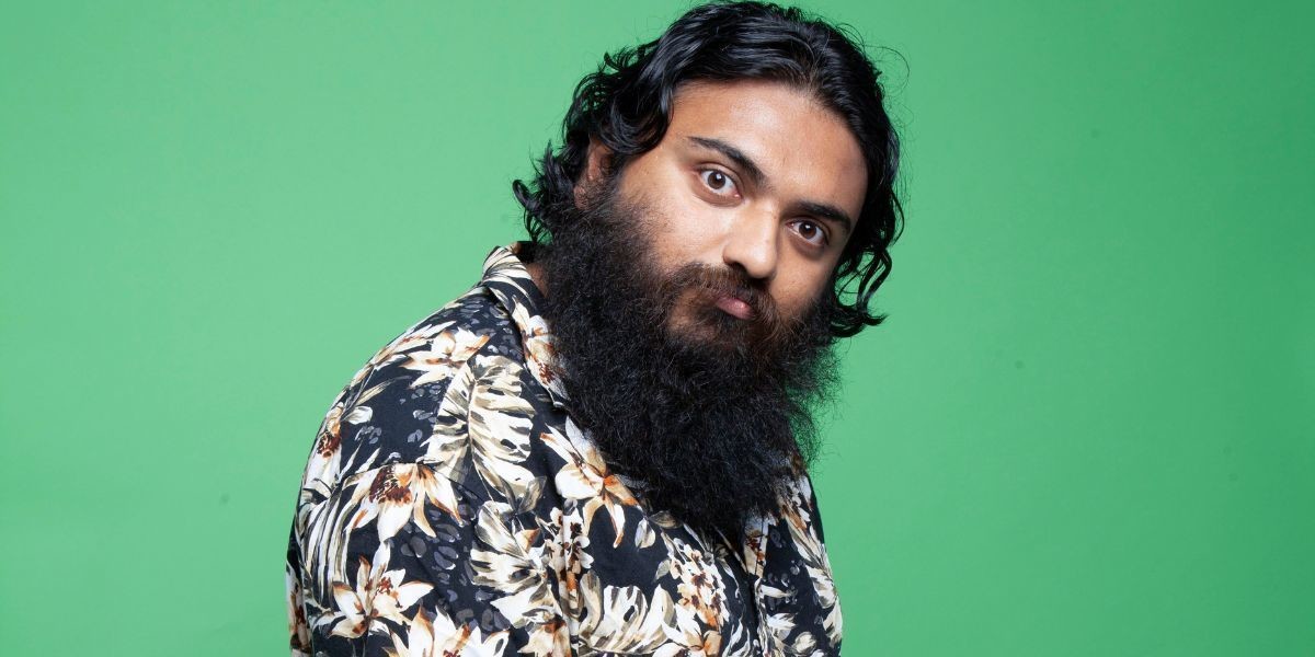 Suraj Kolarkar side on looking at the camera. He is wearing a patterned shirt and the photo is taken on a green background.