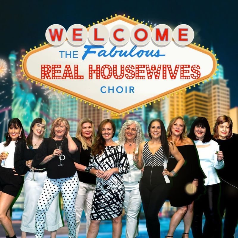 10 women dressed in black and white clothing under an edited Vegas city sign that reads "Welcome The Fabulous Real Housewives Choir" superimposed onto a backdrop of the Vegas Skyline