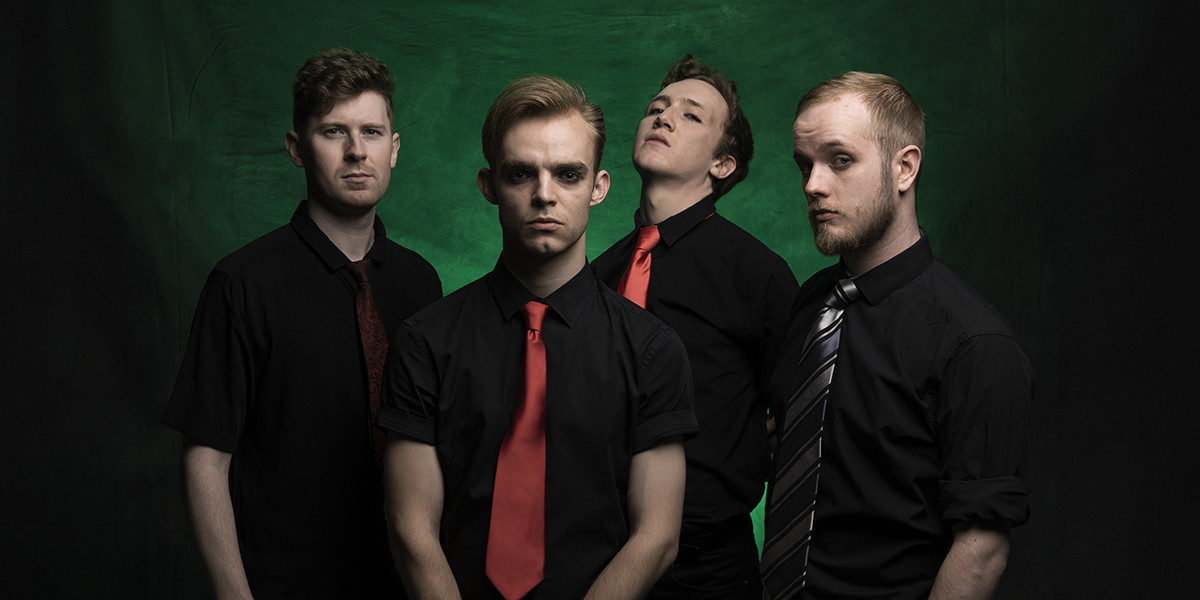 It's Not a Phase! Presents: American Idiot - The four members of the band dressed in black against a green background looking into the camera