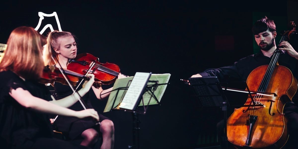 Three musicians, two violins and a cello, play together in a performance.