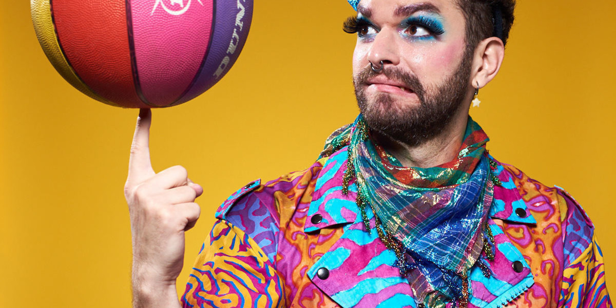 A brightly colored circus performer spins a rainbow basket ball on one finger.