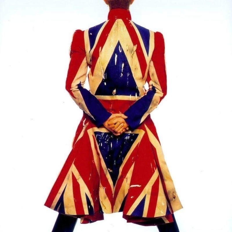 Golden Years and Beyond (1975-2016) - Ashes To Ashes Bowie Tribute - A figure stands against a white background facing away with their hands behind their back and legs apart. They are dressed in a long dress coated made out of the Union Jack, the head and legs from the knee down are cropped out of the image.