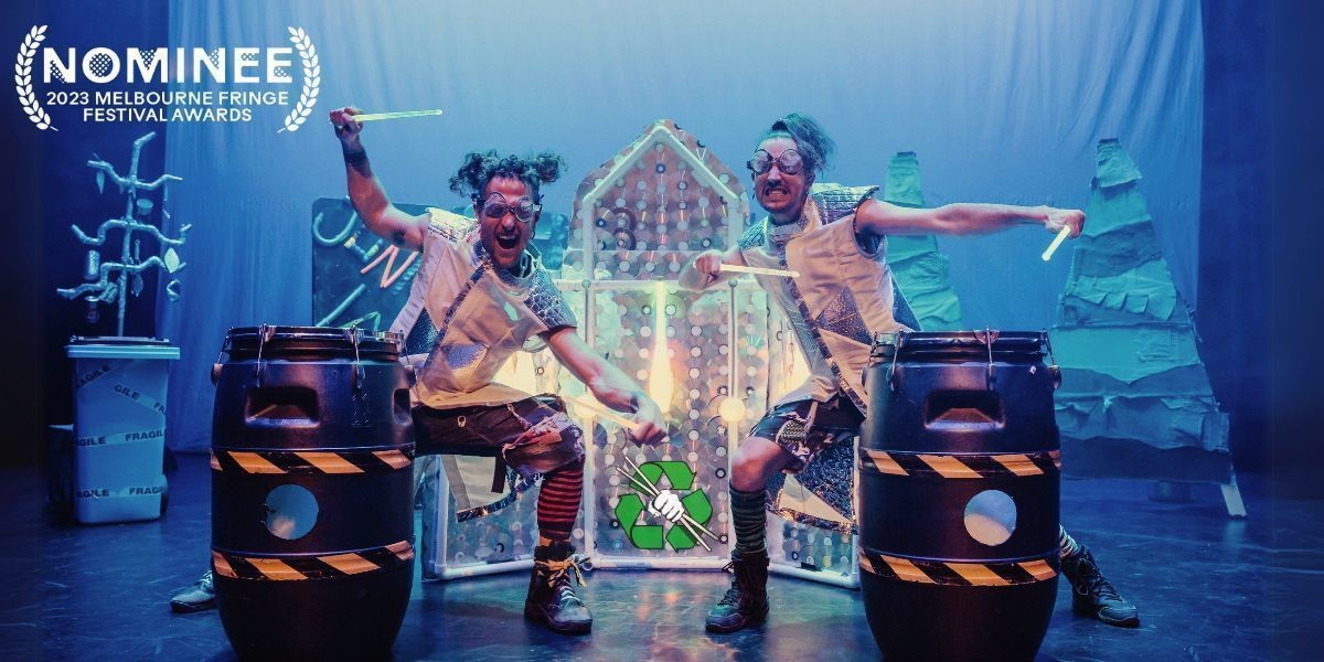 2 brothers dressed in a space costume in front of a spaceship set made out of CD's with LED juggling clubs and poi hanging off it, standing over plastic barrel drums holding LED drumsticks. An upcycled sign at the back says JUNKLANDIA!