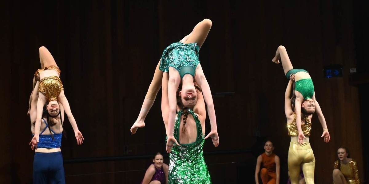 3 partners lifting the smaller person above their head. Wearing gold, blue and green